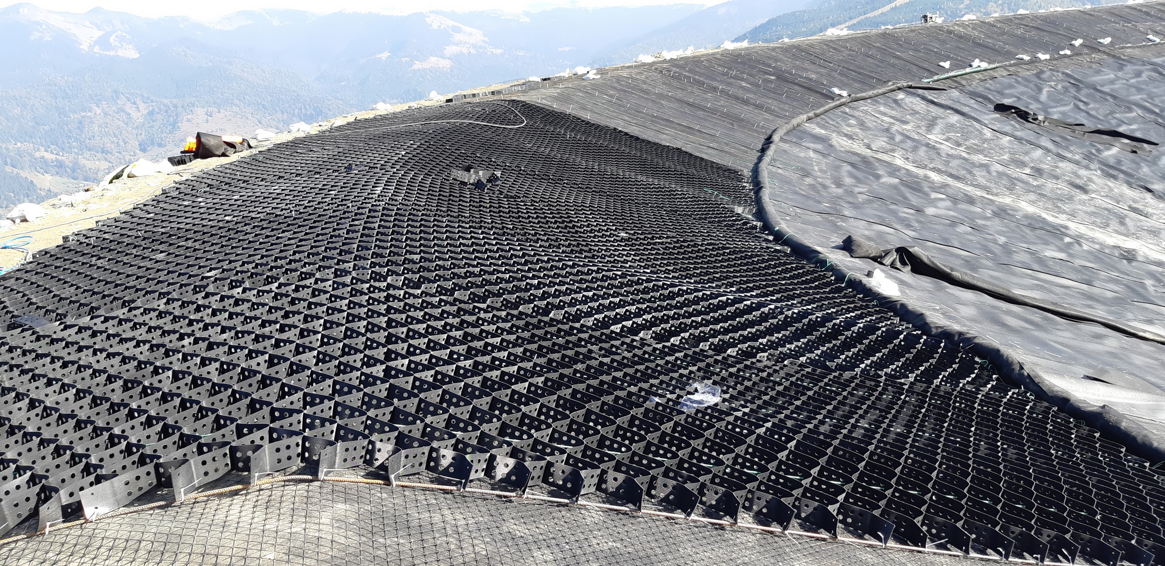 Installation of gravel, triaxial geogrid, and geocells on the lake slopes to provide drainage, confinement, and reinforcement.