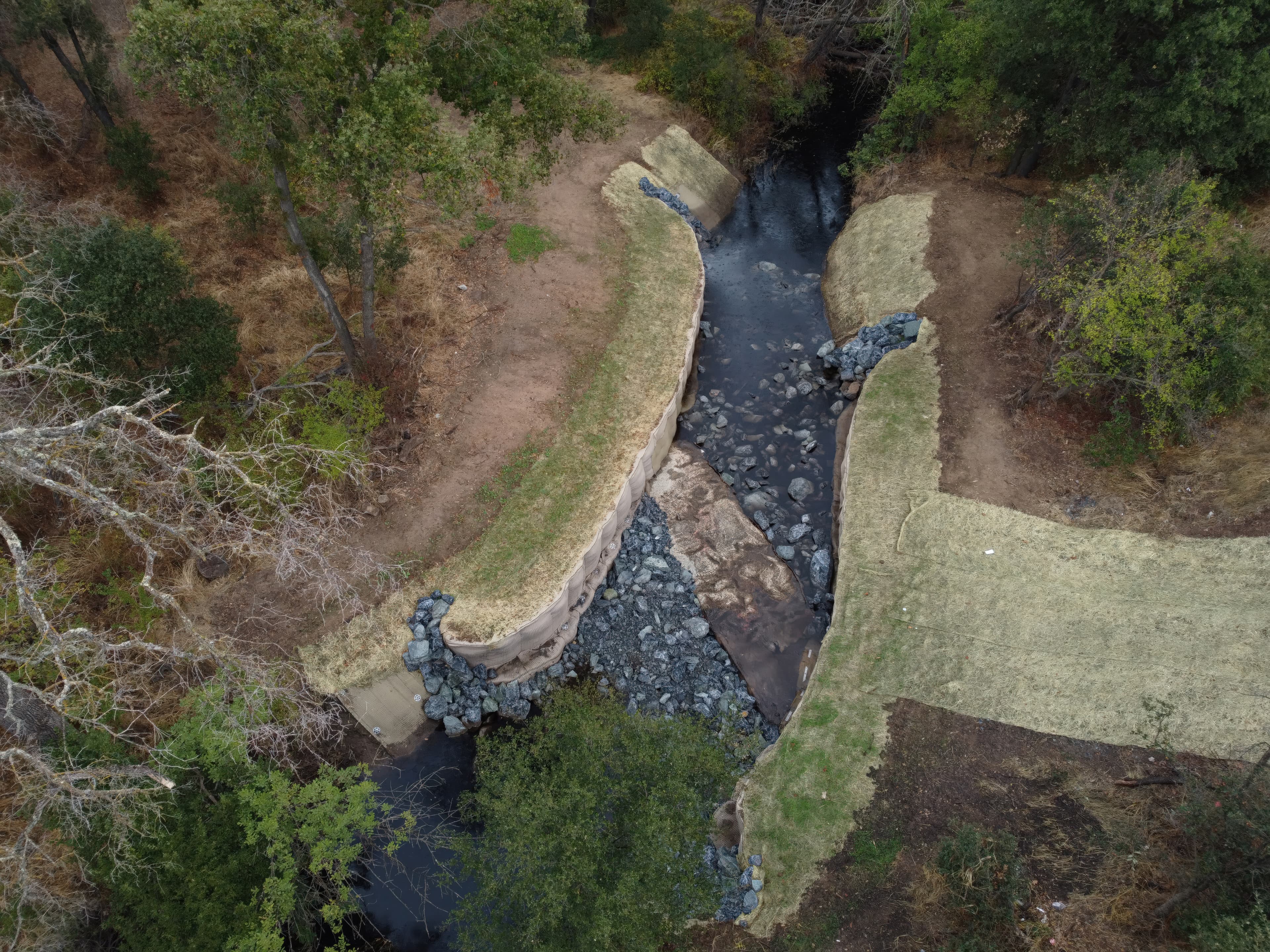 Installation of PROPEX Pyramattress as an adaptable revetment system along a creek bed, shielding exposed pipelines from erosion and hydraulic stresses.